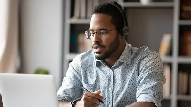 Man holding a pen sits in front of a laptop.