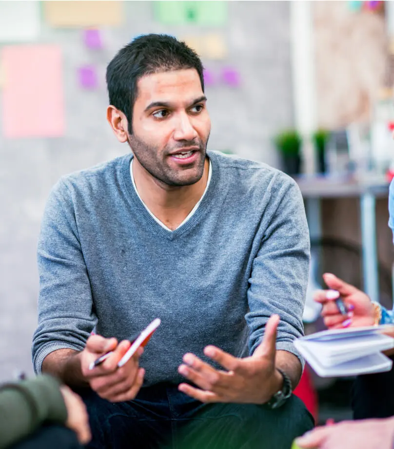 A man holds a notepad and pen in one hand while explaining a point