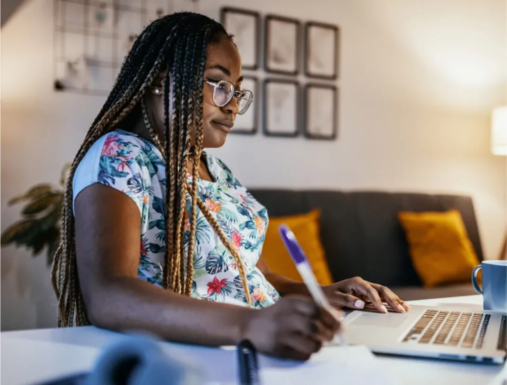 A woman sites at a desk with her laptop and pen
