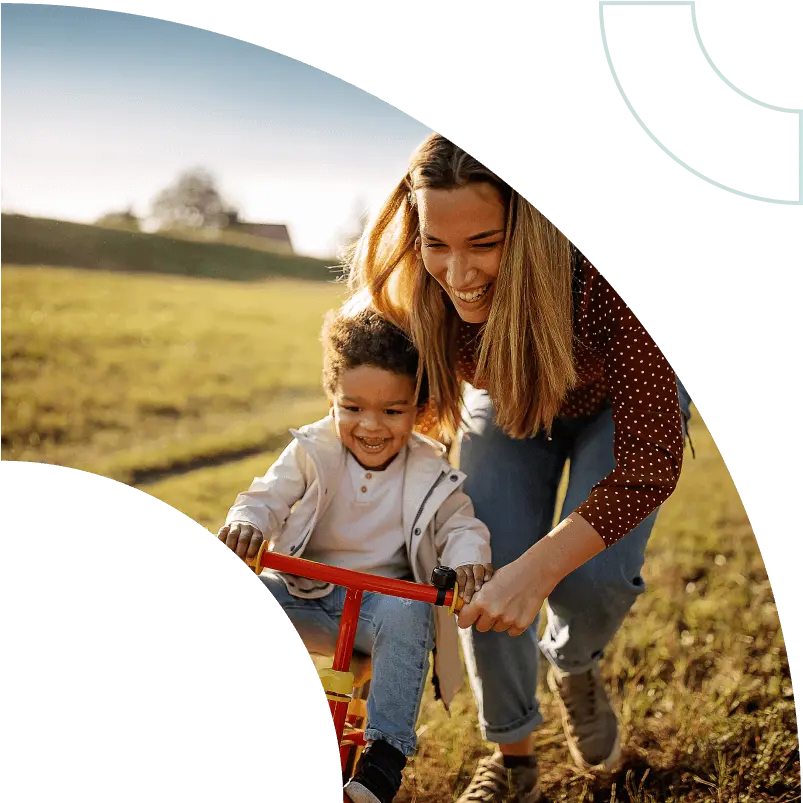 Child rides bike in the grass with a parent