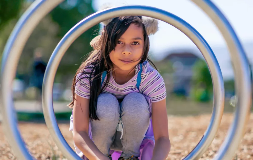 A child crouches and looks at the camera through two metal rings