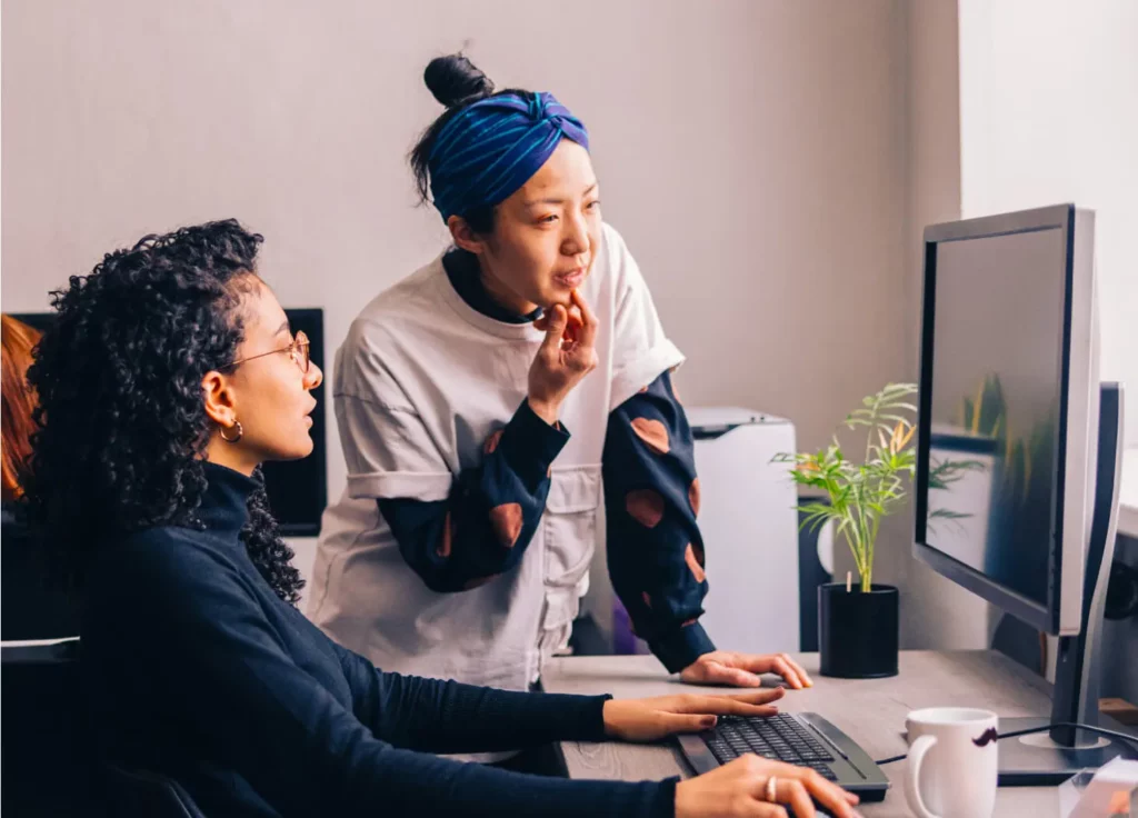 Two women discuss while looking at an external monitor