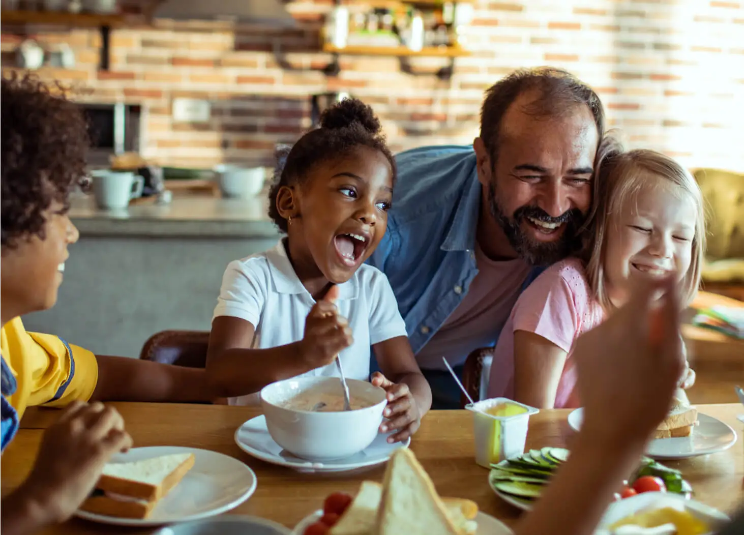 Two kids laugh with a parent at breakfast