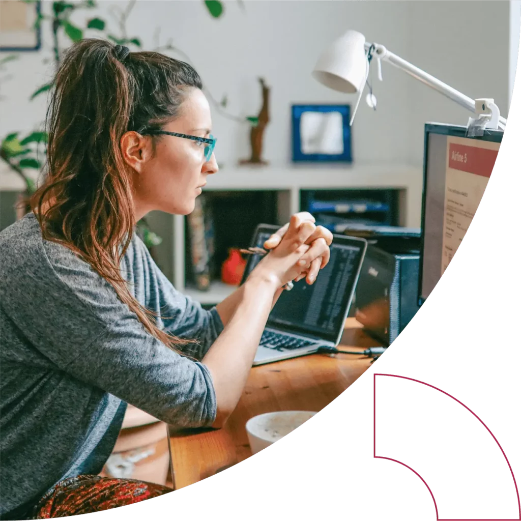 A woman sits at a desk and looks at an external monitor