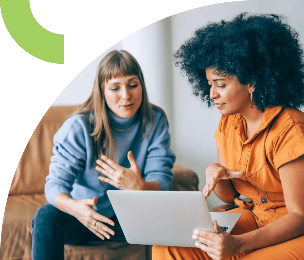 Two people sit with a laptop open while engaging in a discussion.