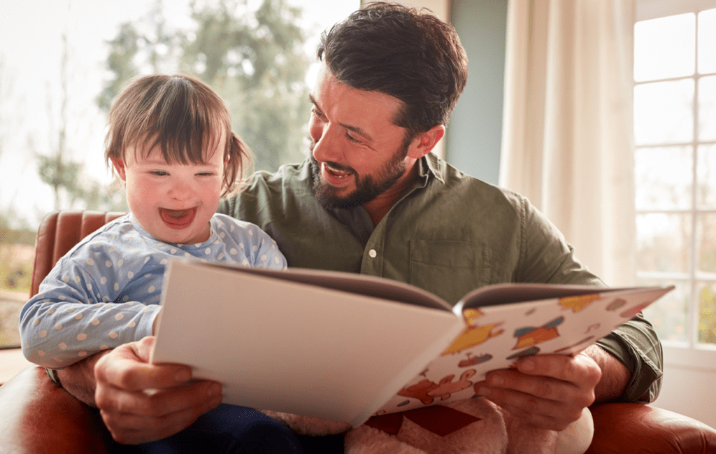 Smiling man and child sitting and reading from an open book.